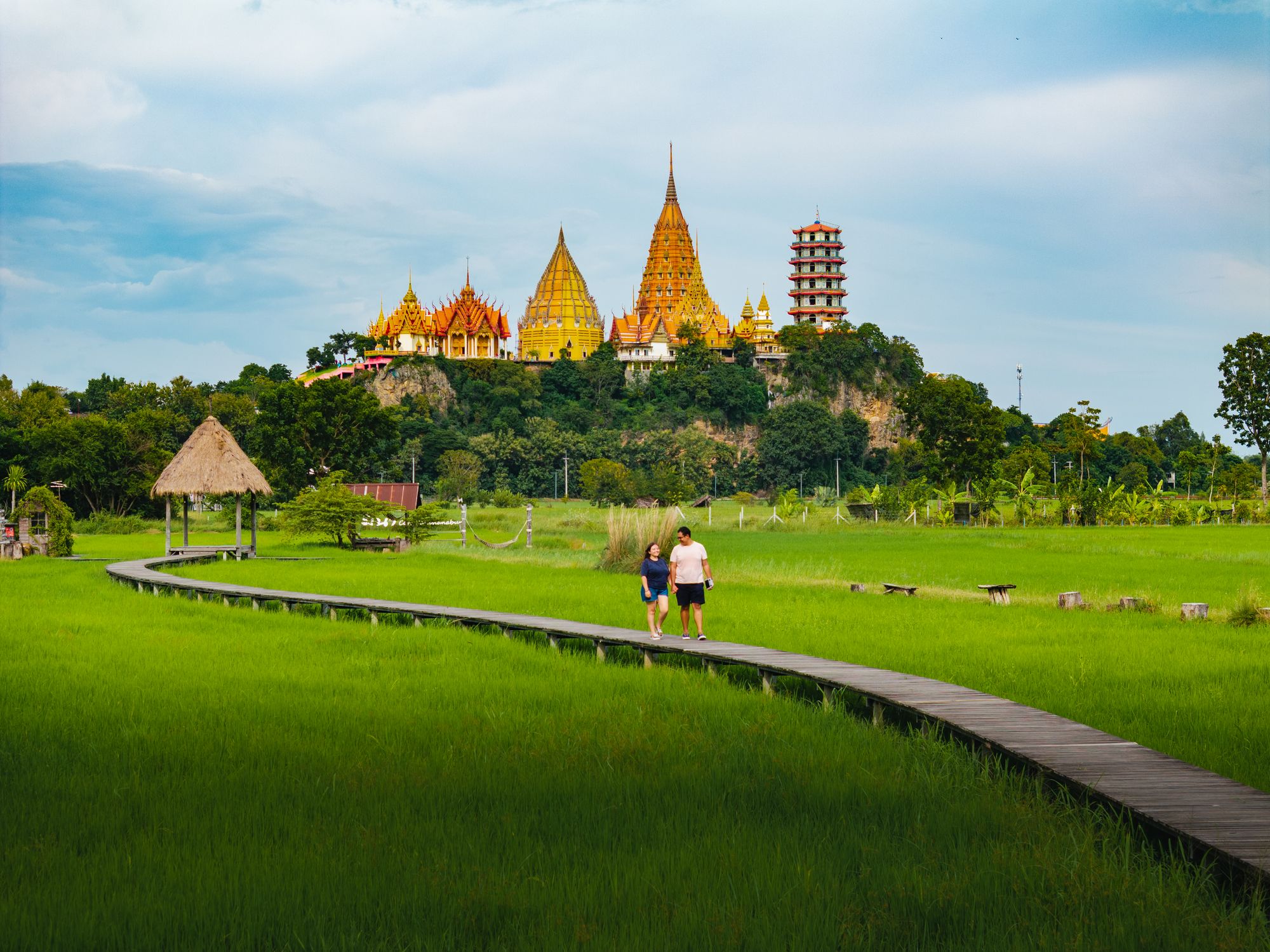 Dos viajeros recorriendo un arrozal frente al templo de Kanchanaburi